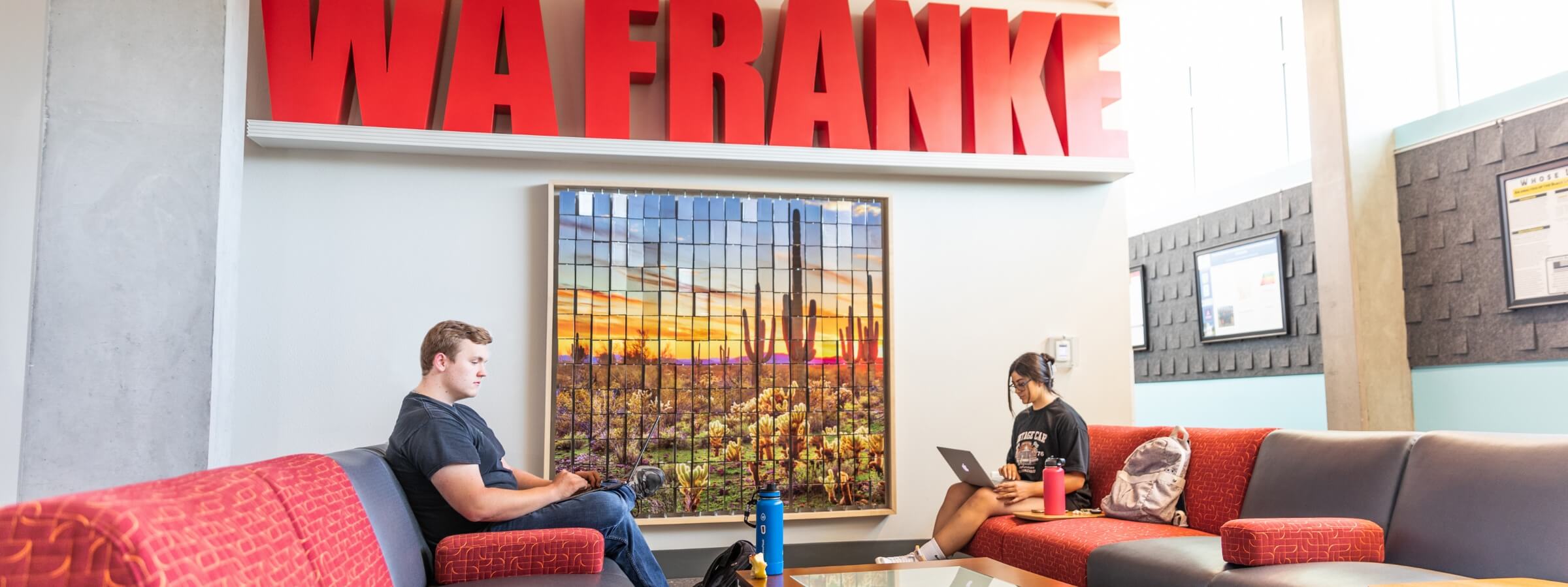 Two students sitting in the WA Franke lounge working on their laptops